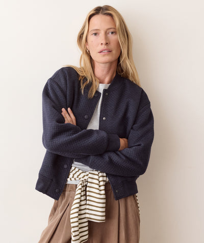 Model wearing a navy Corbet Quilted Bomber jacket with a textured diamond pattern, front view.