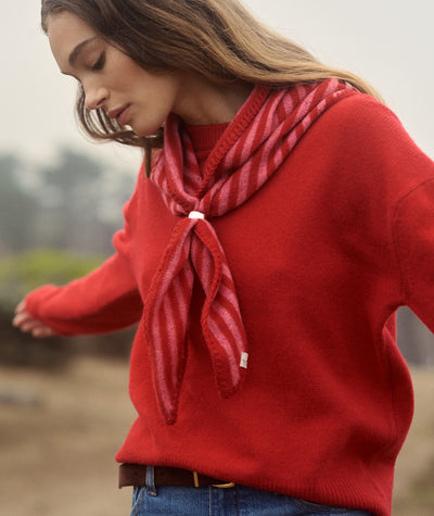 Model wearing a red and pink striped Coastal Merino Triangle Scarf secured with a silver clip.
