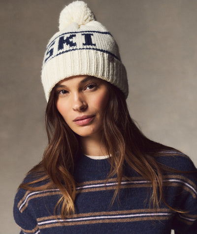 Model wearing a cream and navy Ski Pom Beanie with a pom-pom and striped sweater.