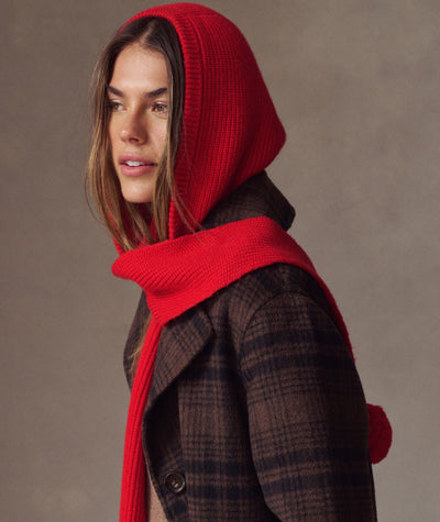 Model wearing a vibrant red knit Snood with hood and scarf design over a brown plaid coat.