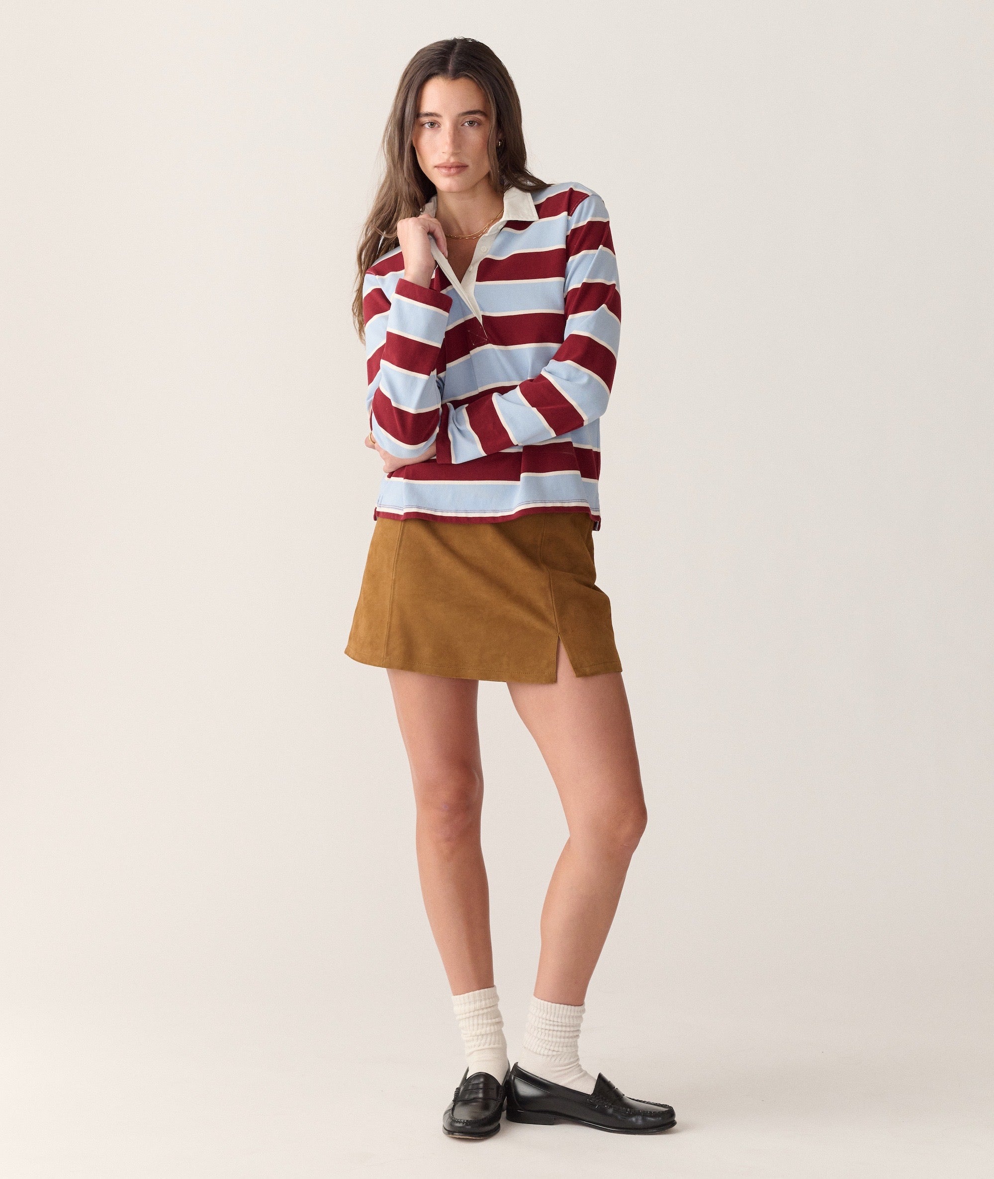 Model wearing the Dream Jersey Rugby Polo in red and blue stripes with a white collar, paired with a skirt.