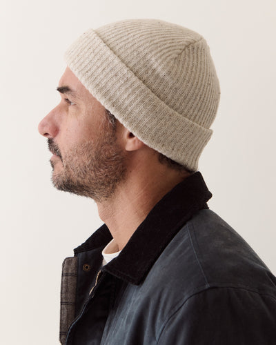 Profile view of a man wearing the cream Coastal Merino Beanie, showcasing its ribbed knit texture.