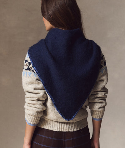 Model wearing a navy blue Coastal Merino Triangle Scarf with blue blanket stitching over a patterned sweater.