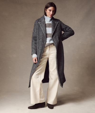 Model wearing the grey herringbone Aspen Coat over a striped sweater and white wide-leg trousers.