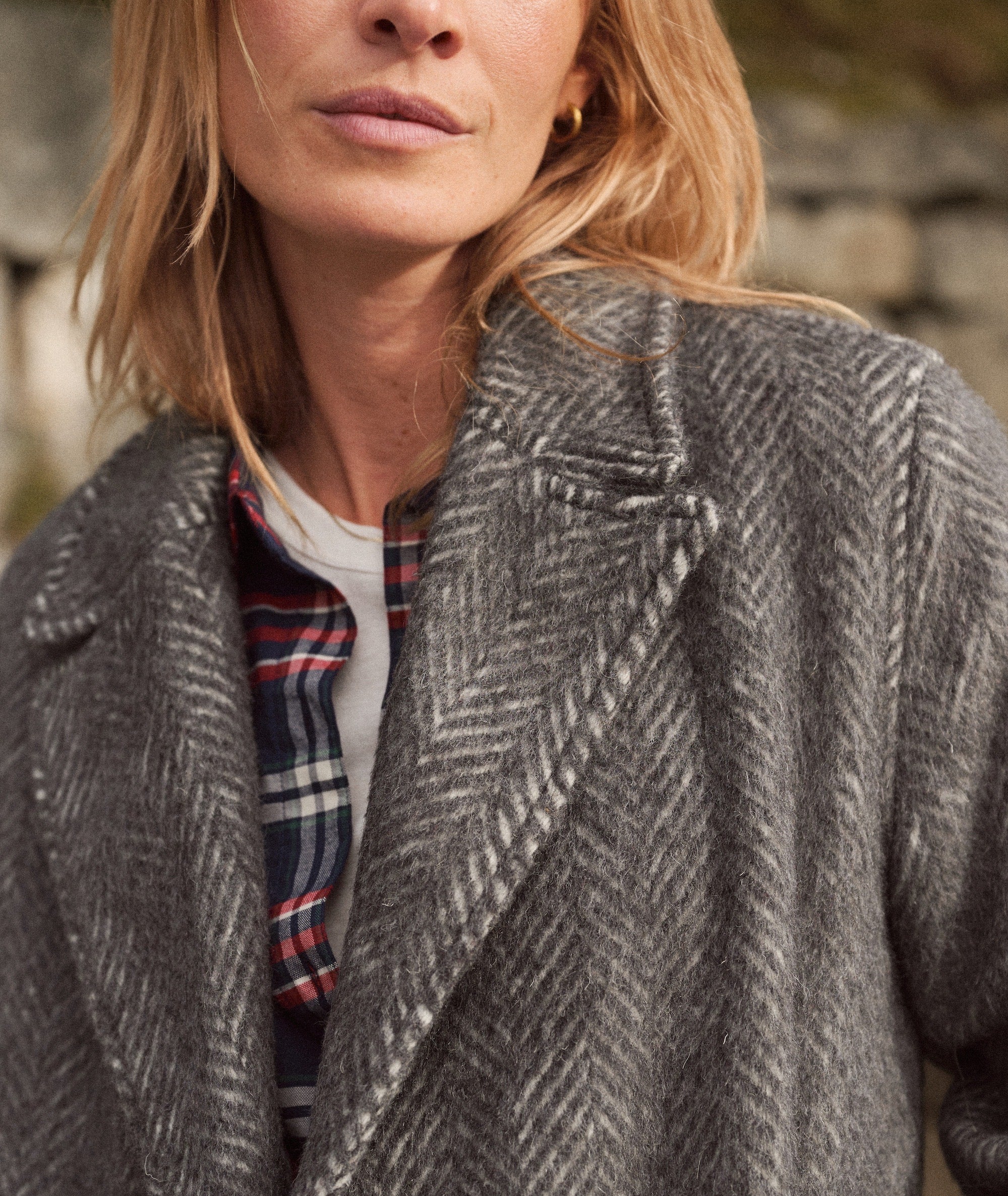 Model wearing the grey herringbone Aspen Coat over a plaid shirt and white tee, close-up view.