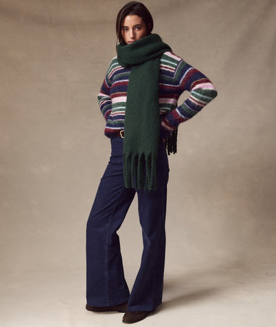 Model wearing a dark green Brushed Scarf with fringe, styled with a striped sweater and dark blue pants.