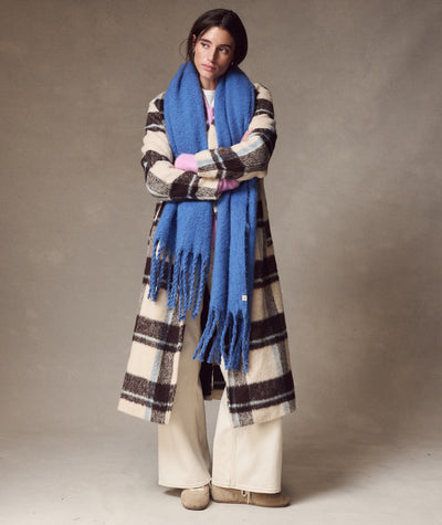 Model wearing a vibrant blue Brushed Scarf with fringe, styled over a plaid coat and cream trousers.