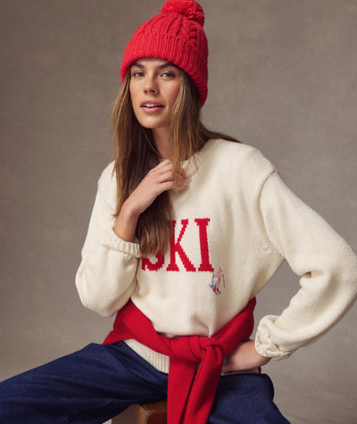 Model wearing a bright red Cable Knit Pom Beanie with a cream ski sweater against a neutral background.