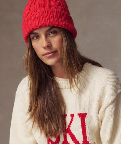 Model wearing a bright red Cable Knit Pom Beanie, close-up view against a neutral background.