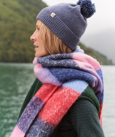 Model wearing a colorful plaid Brushed Scarf, blue beanie, and green sweater outdoors by a lake.