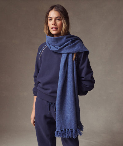 Model wearing a blue Coastal Merino Long Scarf with fringe detail over a matching navy sweatshirt.