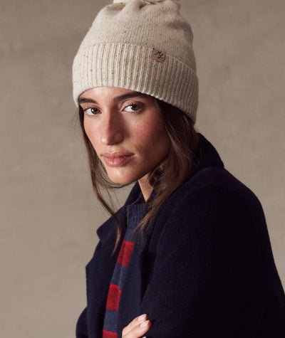 Model wearing a speckled cream Coastal Merino Pom Beanie with a ribbed knit texture and logo tag.