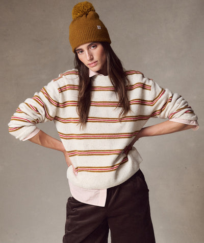 Model wearing a mustard Coastal Merino Pom Beanie with a pom-pom, styled with a striped sweater and shirt.