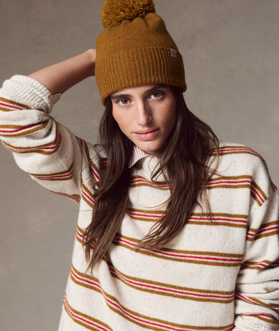 Model wearing a mustard-colored Coastal Merino Pom Beanie with a matching pom-pom and ribbed texture.