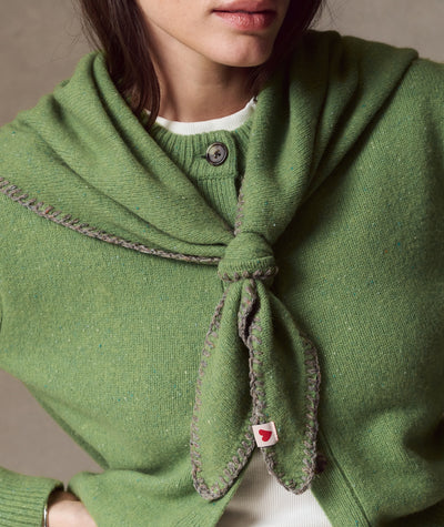 Model wears green Coastal Merino Triangle Scarf with decorative stitching and heart tag over a cardigan.