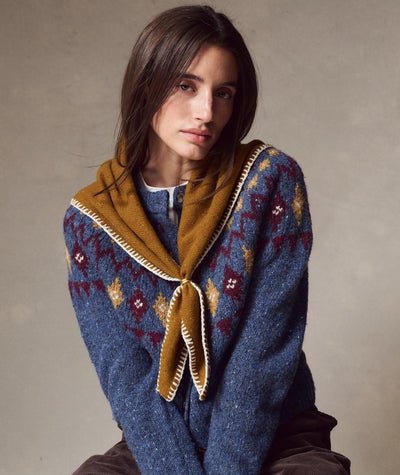 Model wears the mustard Coastal Merino Triangle Scarf with white whipstitch detail over a patterned sweater.