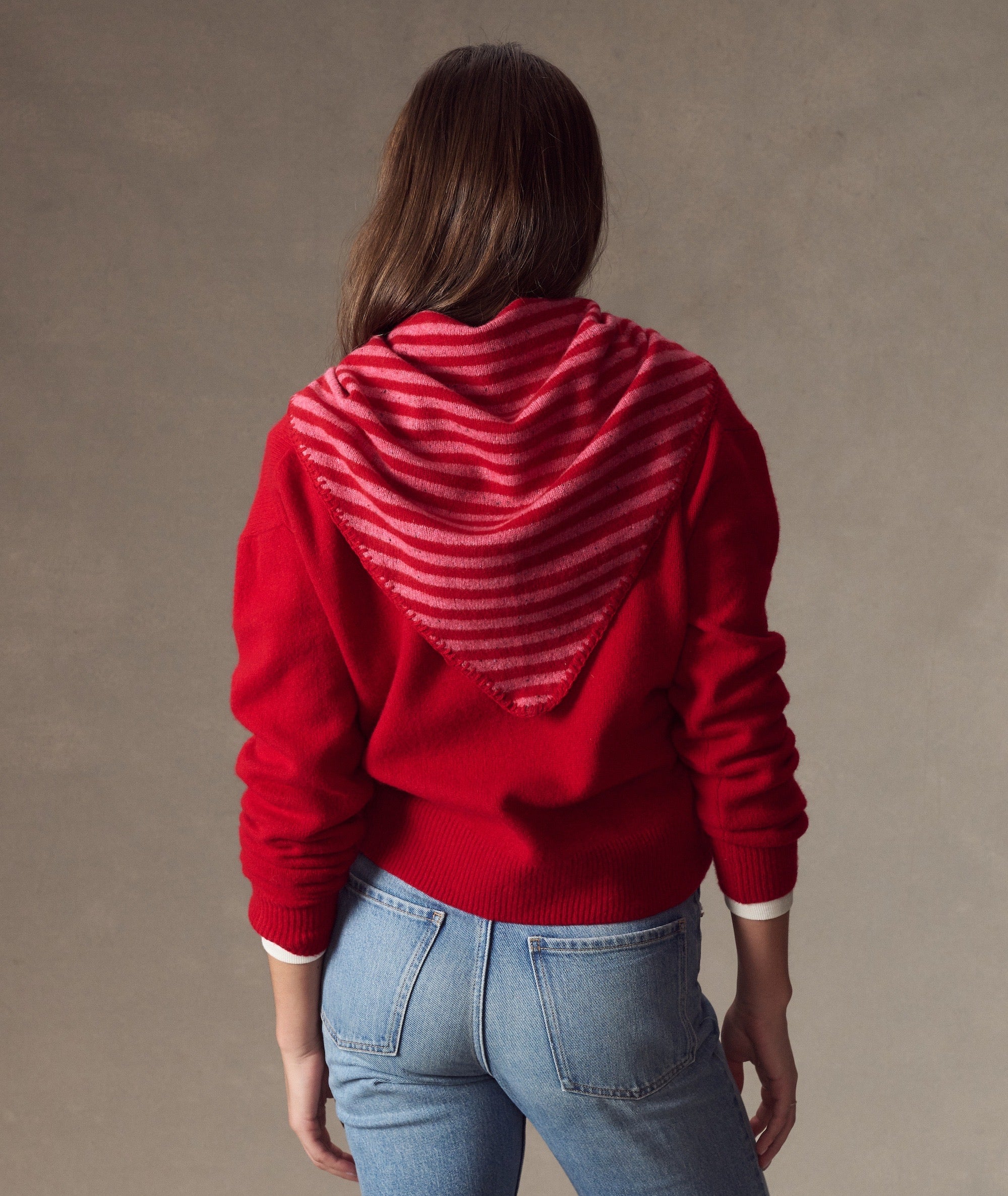 Back view of a model wearing a red and pink striped Coastal Merino Triangle Scarf over a red sweater.