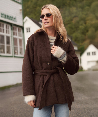 Model wearing a brown Esme Wrap Coat with a tie waist over a striped sweater, outdoors.