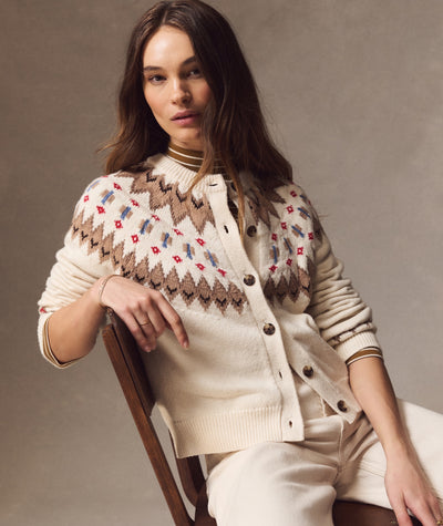 Model wearing cream Fiorella Fair Isle Cardigan with brown and blue geometric patterns, sitting on a chair.