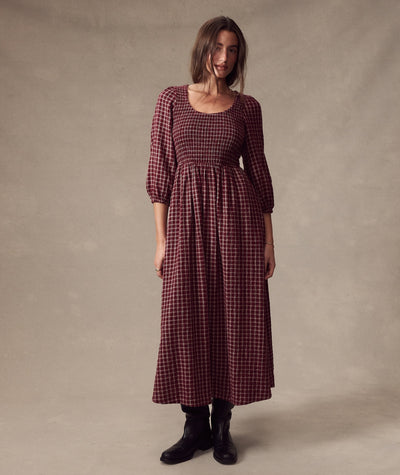 Model wears the burgundy plaid Mari Smocked Dress with a square neckline and black boots.