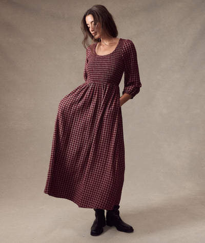 Model wears the burgundy plaid Mari Smocked Dress with long sleeves and pockets, standing against a backdrop.