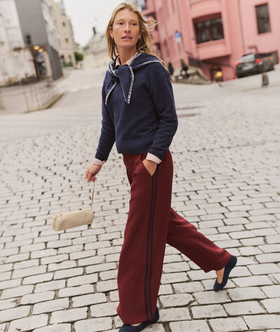 Model wearing burgundy Allison Pleated Wide Leg Trouser with side stripes, paired with a navy sweater.