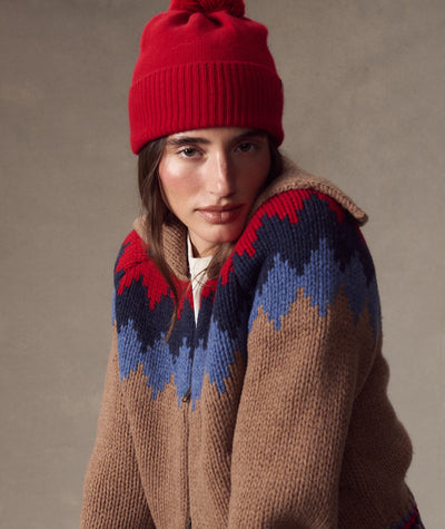 Model wearing a red Coastal Merino Pom Beanie with a matching pom-pom, styled with a patterned sweater.