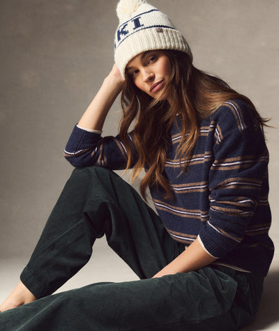 Model wearing a cream and navy Ski Pom Beanie with a pom-pom, styled with a striped sweater.