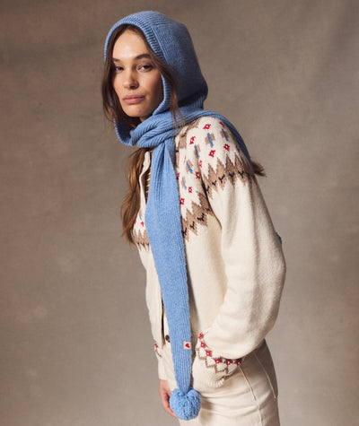 A model wears a light blue ribbed Snood with a pom-pom detail, styled over a patterned cream cardigan.