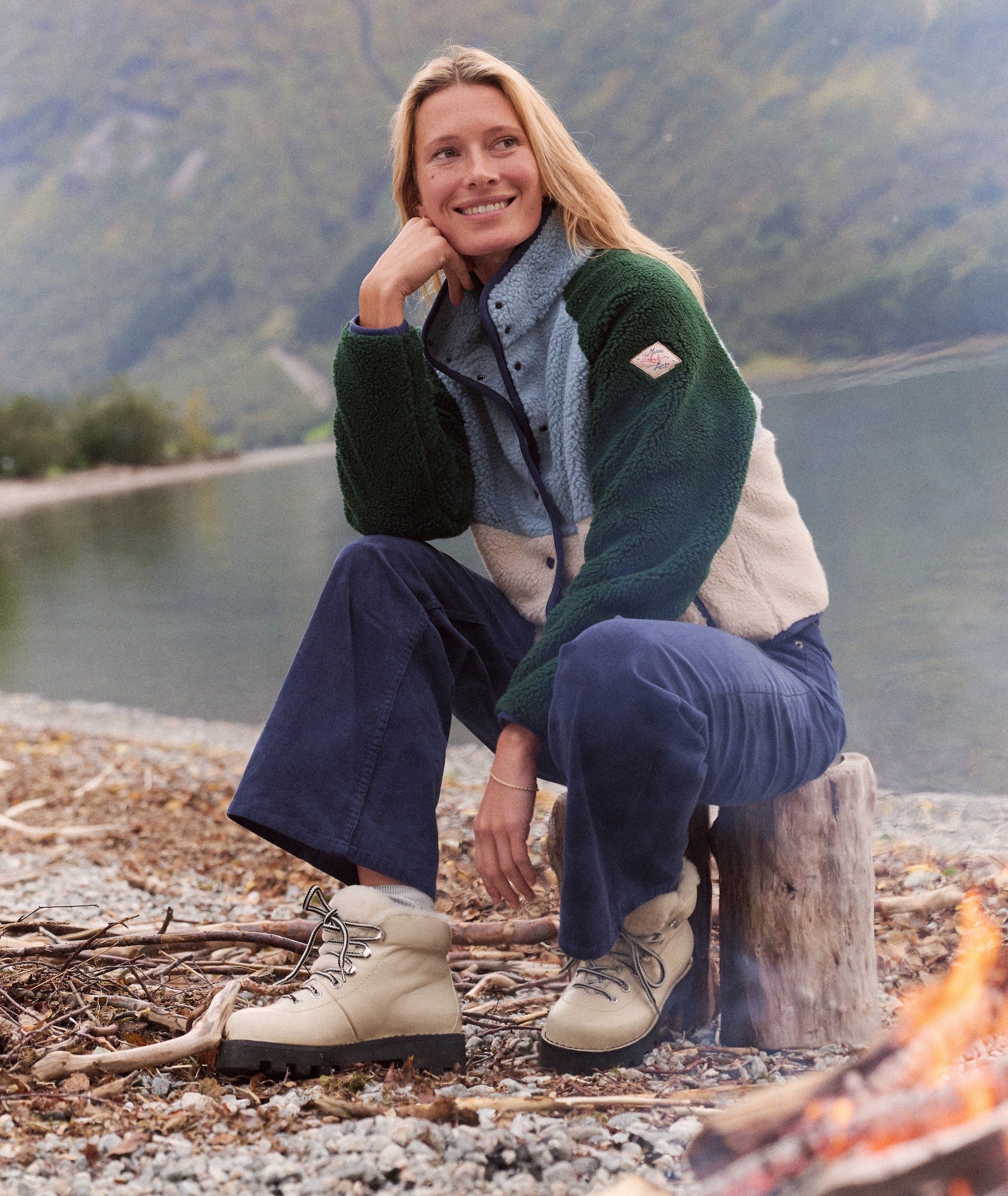 Model wearing the color-blocked Dara Sherpa Jacket while sitting outdoors by a fire.