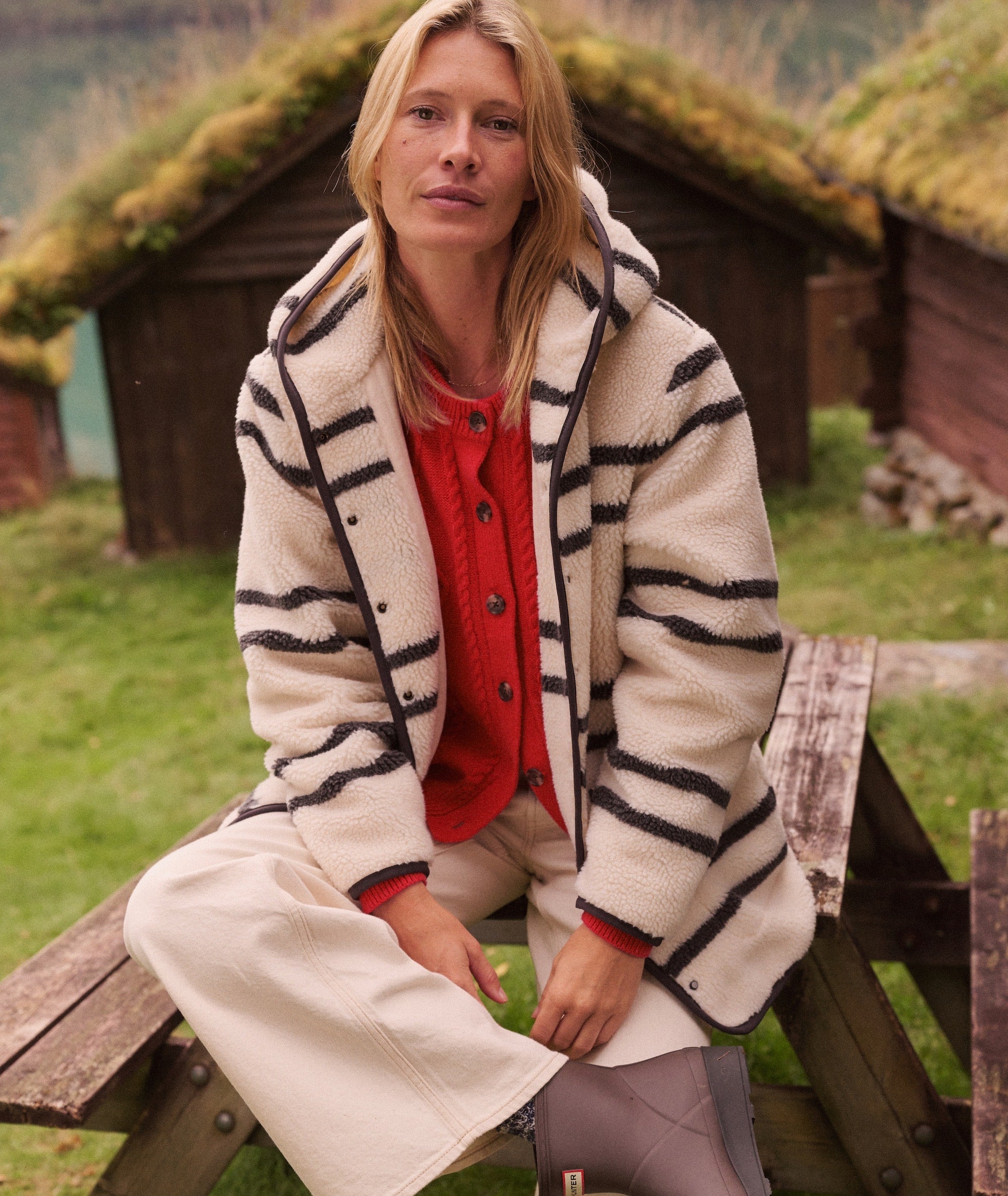 Model wearing the cream and black striped Lennox Sherpa Jacket with a hood, sitting outdoors.