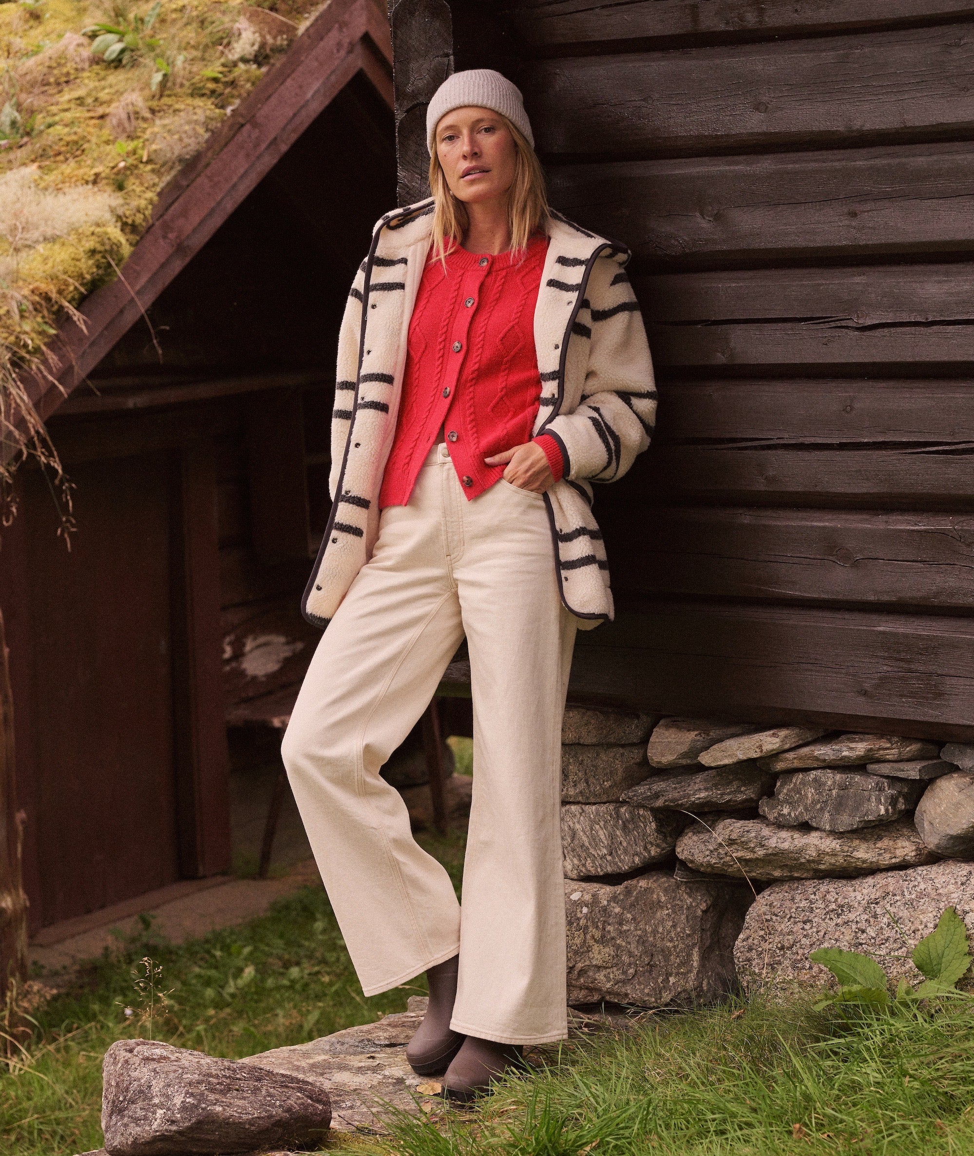 Model wearing the cream Lennox Sherpa Jacket with black stripes, red cardigan, and cream wide-leg pants.