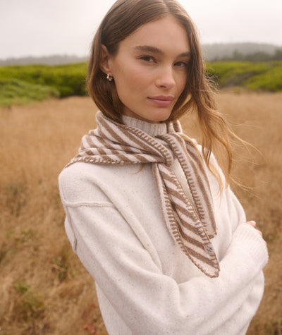 Model wearing a tan and white striped Coastal Merino Triangle Scarf with blanket stitching in a field.