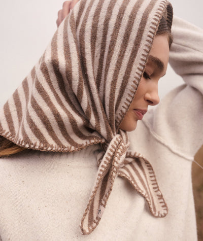 Model wearing a brown and cream striped Coastal Merino Triangle Scarf with blanket stitching.